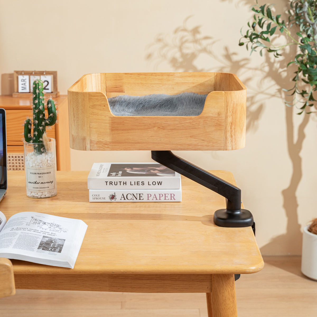 Catomi desk cat bed in Natural raised on its arm above a desk with books and a cactus