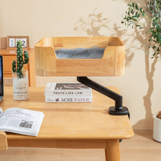 Catomi desk cat bed in Natural raised on its arm above a desk with books and a cactus